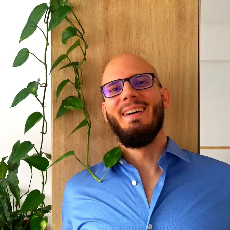 Profile picture of Bálint Kiss in blue shirt behind a houseplant